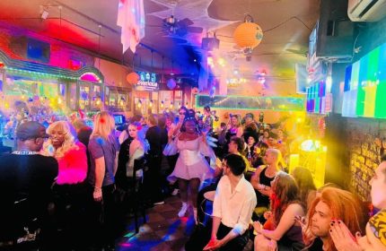 Suite Bar, NYC gay pub, Halloween party. People enjoy the festive atmosphere, with colorful lights and decorations. Gay travel in New York.