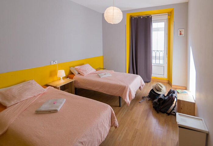 Sungate One, Madrid gay hostel in Chueca. Room with two beds, yellow accents, and a backpack. A great option for gay travelers.