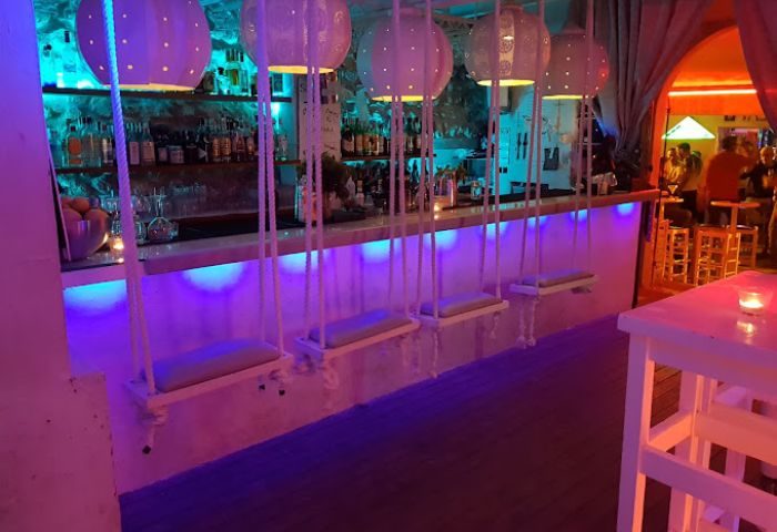 Sunrise gay bar in Ibiza. Swings as seats at the bar, illuminated with neon lights. Gay travel destination.