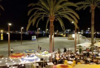Night view of Ibiza's gay bar scene. Palm trees, lights, and people enjoying the vibrant atmosphere. Gay travel in Ibiza at its finest.