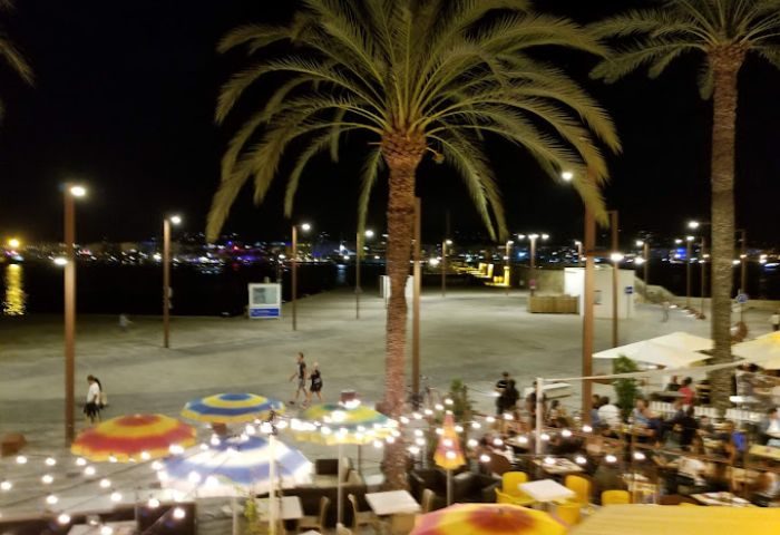 Night view of Ibiza's gay bar scene. Palm trees, lights, and people enjoying the vibrant atmosphere. Gay travel in Ibiza at its finest.