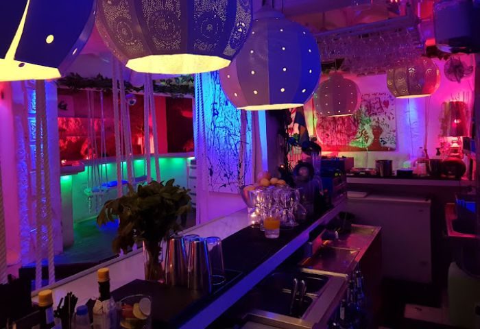 Interior of a vibrant gay bar in Ibiza. Colorful lights, hanging lamps, and a well-stocked bar create a fun, welcoming atmosphere. Gay travel.
