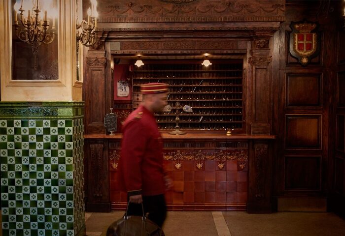 The Jane Hotel's lobby in NYC, a super-cool hotel for gay travelers. A bellhop walks past the reception desk. The hotel has a vintage aesthetic.