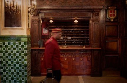 The Jane Hotel's lobby in NYC, a super-cool hotel for gay travelers. A bellhop walks past the reception desk. The hotel has a vintage aesthetic.