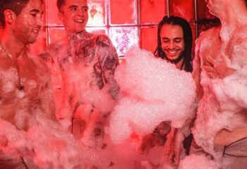 Sweatbox sauna in London. Four gay men enjoy a foam party in the red-lit sauna. Gay travel advice.
