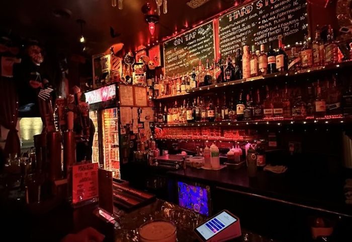 Sweaty Betty's Bar interior in Toronto. A dimly lit, lively gay bar with a fully stocked bar and a chalkboard menu. Gay travel destination.