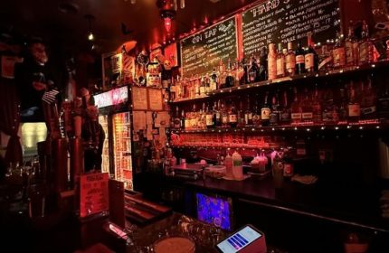 Sweaty Betty's Bar interior in Toronto. A dimly lit, lively gay bar with a fully stocked bar and a chalkboard menu. Gay travel destination.