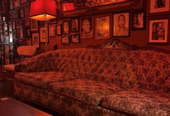Sweaty Betty's Bar in Toronto: Red-toned interior with vintage couch, lamp, and framed photos. Gay bar known for its cozy, eclectic atmosphere.