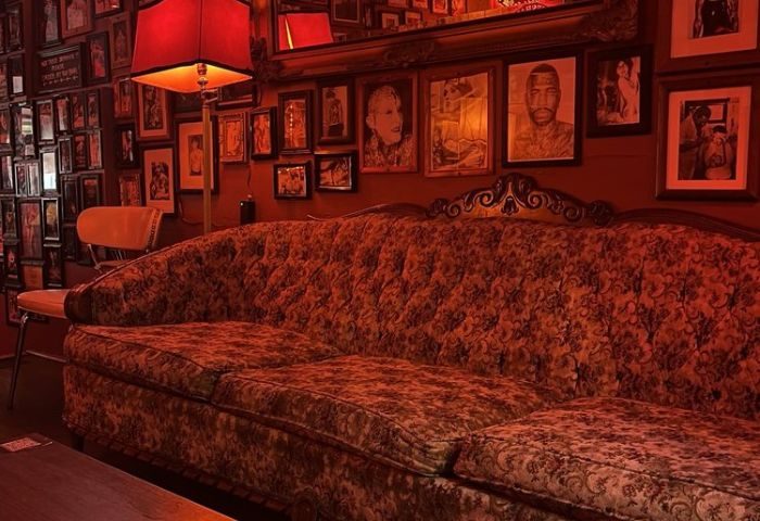 Sweaty Betty's Bar in Toronto: Red-toned interior with vintage couch, lamp, and framed photos. Gay bar known for its cozy, eclectic atmosphere.
