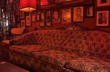 Sweaty Betty's Bar in Toronto: Red-toned interior with vintage couch, lamp, and framed photos. Gay bar known for its cozy, eclectic atmosphere.