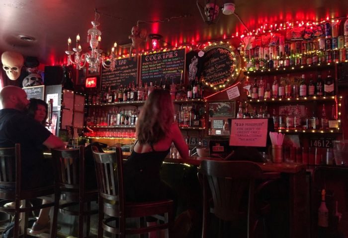 Sweaty Betty's Bar in Toronto. People at the bar, shelves of bottles, and red lights. A unique bar for gay men's travel adventures.