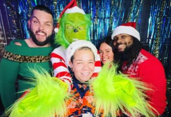 Sweetwater Saloon Fun: Group of diverse people at a gay bar, including one in a Grinch costume, celebrating a holiday with festive attire.