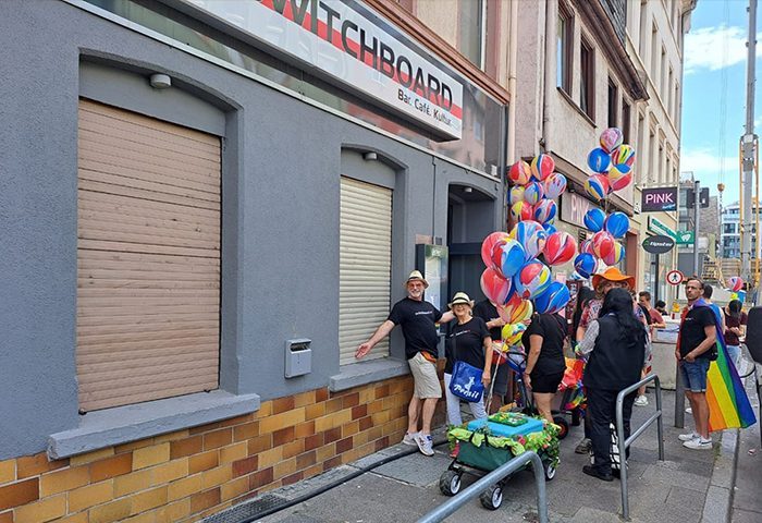 Switchboard Frankfurt: Gay bar with closed shutters, colorful balloons, and people celebrating on the street. Gay travel advice.