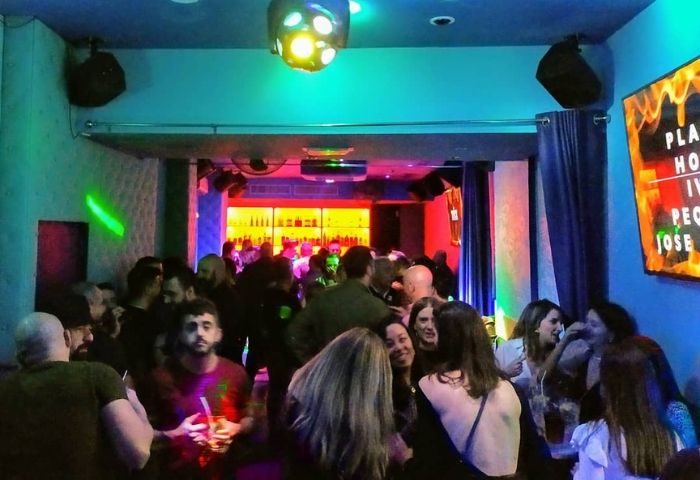 Crowded gay bar in Madrid. Patrons mingle under colorful lights. A lively nightlife scene with drinks and music. Gay travel destination.