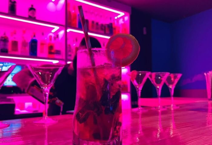 Cocktail at THICK Gay Bar in Madrid. Pink neon lights illuminate drinks on the bar. Gay travel nightlife scene.