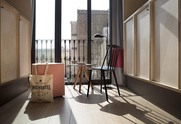 TOC Hostel Barcelona room with chair, table, and balcony view. Best gay hostel in Eixample gayborhood for nightlife. Stylish interior.