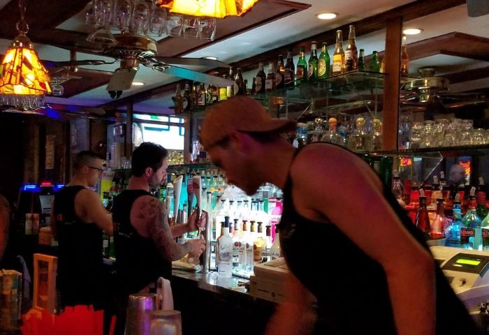 TRUNKS Experience: Bartenders at a gay bar. Bottles line the shelves. Ceiling fans and lamps add to the ambiance. Gay travel advice.