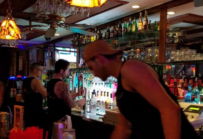TRUNKS Experience: Bartenders at a gay bar. Bottles line the shelves. Ceiling fans and lamps add to the ambiance. Gay travel advice.
