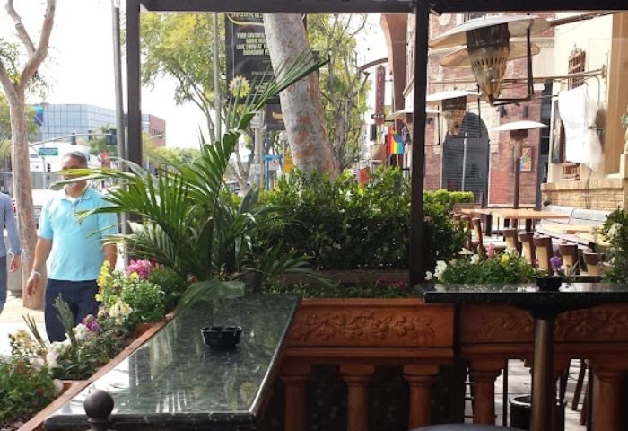 Outdoor patio at TRUNKS bar in West Hollywood, CA, a gay-friendly travel destination. Morning light, plants, and tables visible.