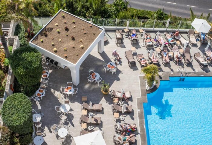 Aerial view of TUI Blue Gardens, an adults-only, gay-friendly hotel in Madeira. Pool, sun loungers, tables, and bar area visible. Savoy Signature.