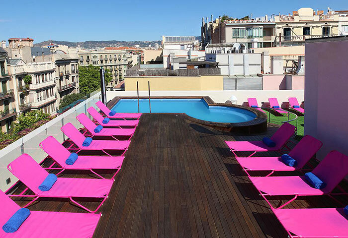 Rooftop pool at TWO Hotel Barcelona by Axel, adults only gay hotel. Pink loungers, wooden deck, city view. Most wanted gay destination.