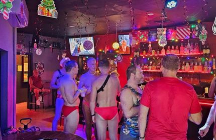 Gay Waikiki: Honolulu's Tapas bar scene. Men in swimwear enjoy drinks at a gay bar with festive decor. Nightlife in Honolulu, Hawaii.