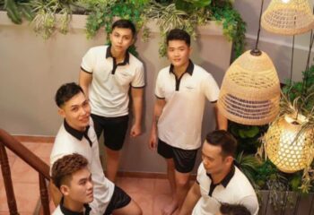 Gay travel: Tarzan Spa Ho Chi Minh City staff. Five Asian men in matching uniforms pose indoors. Spa lighting and greenery visible.