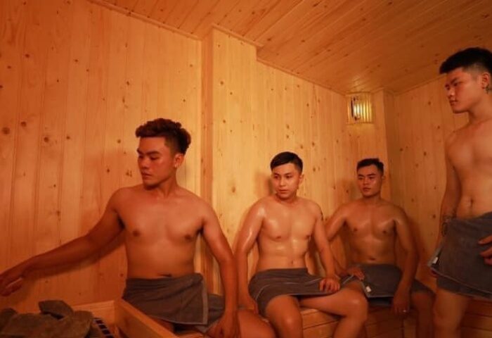 Gay sauna at Tarzan Spa, Ho Chi Minh City. Four shirtless men in towels relax in a wood-paneled sauna. Gay travel advice.