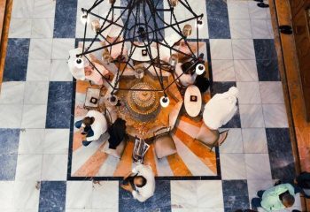 Overhead view of Galatasaray Hamami in Istanbul. People relax around a central platform beneath a chandelier. Marble tile floor. Gay travel destination.