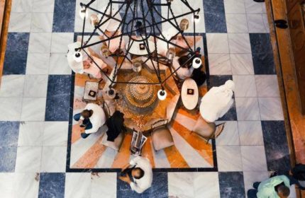 Overhead view of Galatasaray Hamami in Istanbul. People relax around a central platform beneath a chandelier. Marble tile floor. Gay travel destination.