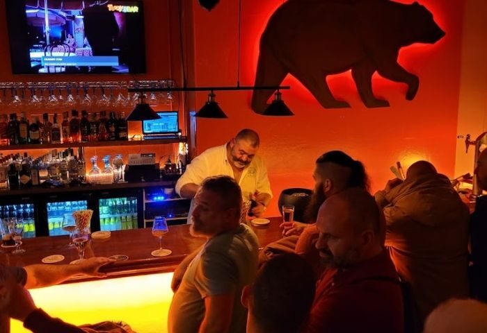 Teddy Bar, a gay bar in Barcelona. Bartender serving drinks at the counter, bear silhouette on the wall. Gay travel advice.
