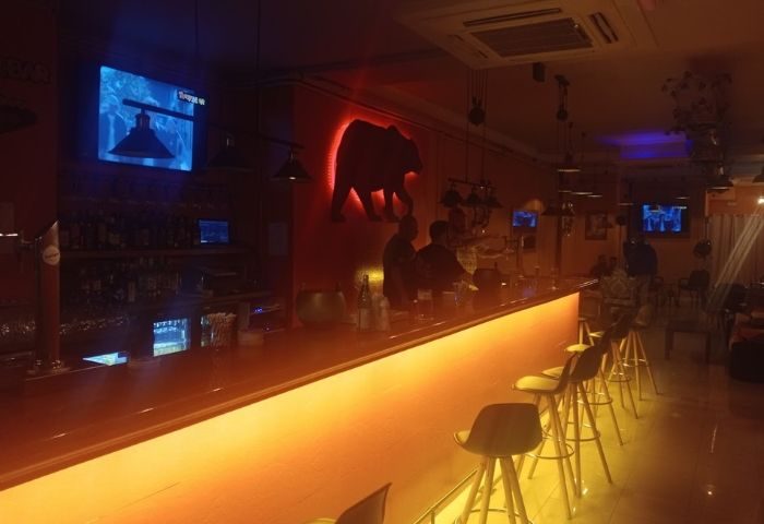 Interior of Teddy Bar, a gay bar in Barcelona. Long, illuminated bar with stools, TVs, and a bear silhouette on the wall. Nightlife.