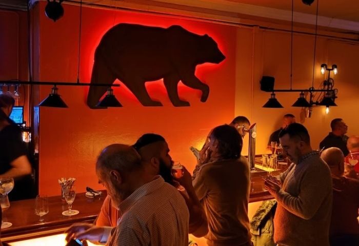 Interior of Teddy Bar, a gay bar in Barcelona. A bear silhouette is on the wall above patrons at the bar. Gay travel destination.