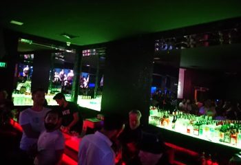 Tek Yon Club Istanbul bar scene. Gay men gather at the bar in the Istanbul nightclub with green and red lighting, mirrored walls.