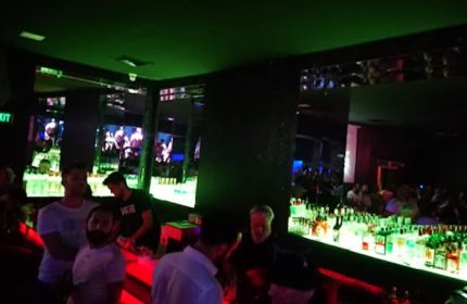 Tek Yon Club Istanbul bar scene. Gay men gather at the bar in the Istanbul nightclub with green and red lighting, mirrored walls.