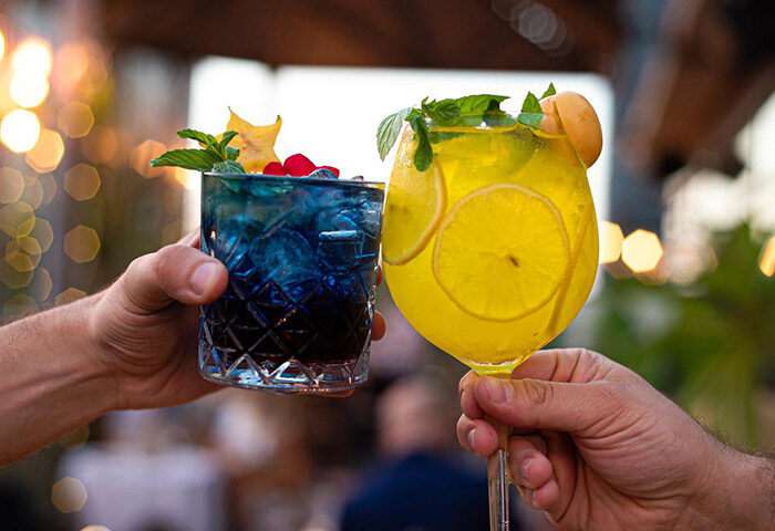 Inta Hotel Tel Aviv Jaffa: Two hands toasting colorful cocktails at the bar. Adults-only gay hotel in Tel Aviv, Israel.