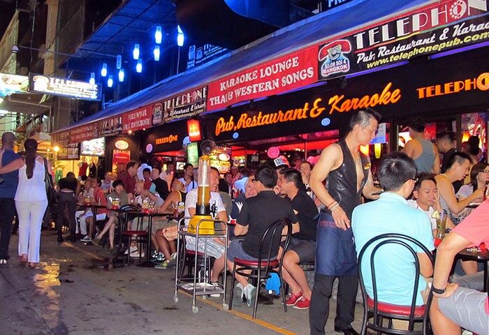 Telephone Pub Restaurant, a popular gay bar in Silom, Bangkok. Outdoor seating area filled with patrons enjoying drinks and karaoke. Nightlife scene.