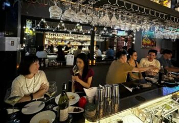 Terroir Wine Bar, Ho Chi Minh City. People enjoy wine at the bar. Glasses hang above. A vibrant nightlife spot for gay travelers.