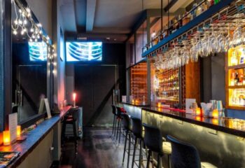 Interior of Terroir Wine Bar in Ho Chi Minh City, Vietnam. Bottles line shelves behind the bar. Glasses hang above. Gay travel advice.