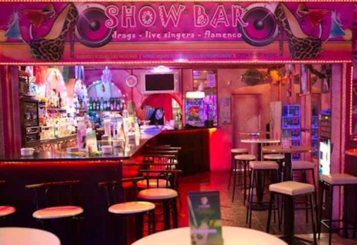 Terry's Show Bar, a gay bar in Gran Canaria, Spain. Pink neon sign, bar stools, and tables create a vibrant, inviting atmosphere.