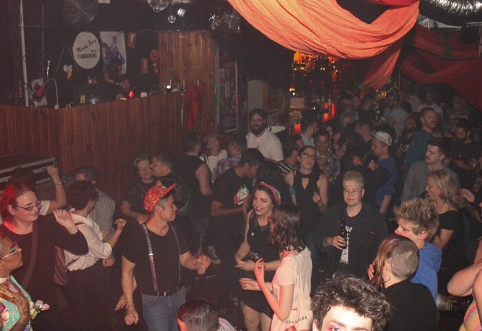 The 86 Melbourne: Gay men dancing at a crowded club. Orange fabric hangs from the ceiling. Disco balls reflect light. Nightlife travel.