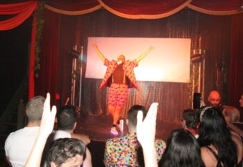 Melbourne, Australia: Drag queen on stage at The 86, a gay bar. Audience members with hands raised. Gay travel advice.