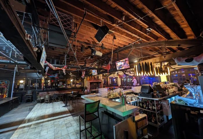 Interior of The Abbey Bar, a gay bar. The bar area is visible, with bottles and glasses. The ceiling has exposed wooden beams and lighting fixtures.