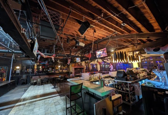Interior of The Abbey Bar, a gay bar. The bar area is visible, with bottles and glasses. The ceiling has exposed wooden beams and lighting fixtures.