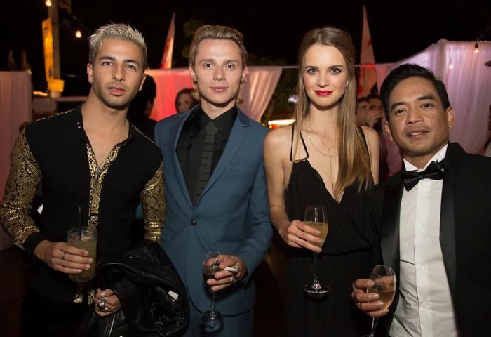 Four people at The Abbey Celebration, a gay bar. Men in suits and a woman in a black dress hold drinks. Gay travel advice.