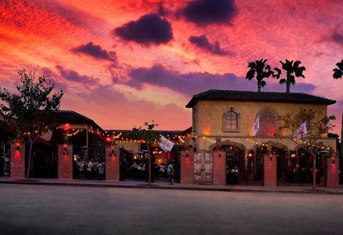 The Abbey location exterior at sunset. Gay bar with string lights, palm trees, and a vibrant sky. Gay travel destination.