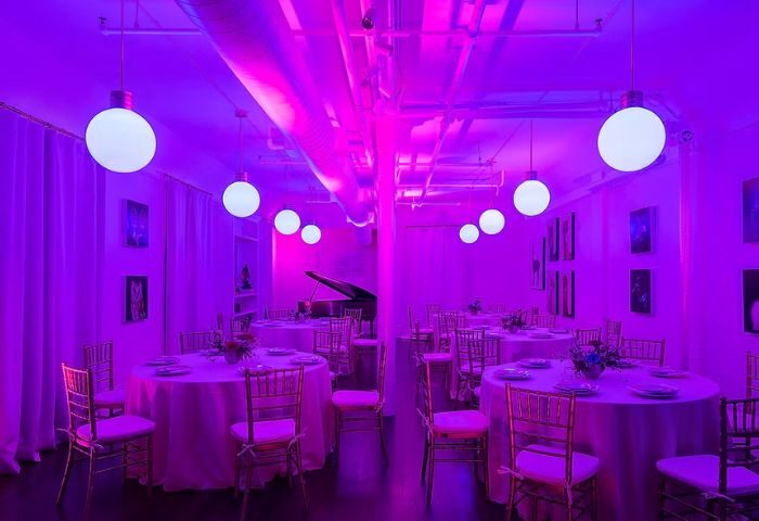 The Academy Social Club in San Francisco: Interior view of the club with round tables, chairs, and a piano, all bathed in vibrant purple light.