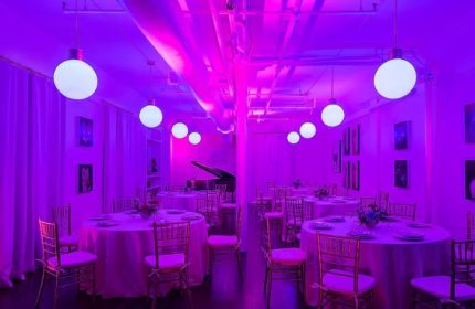 The Academy Social Club in San Francisco: Interior view of the club with round tables, chairs, and a piano, all bathed in vibrant purple light.