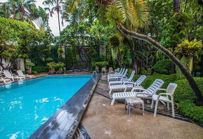 Babylon Bangkok Hotel pool. Best gay hotel with sauna. Tropical trees surround lounge chairs by the pool. Gay travel in Thailand.
