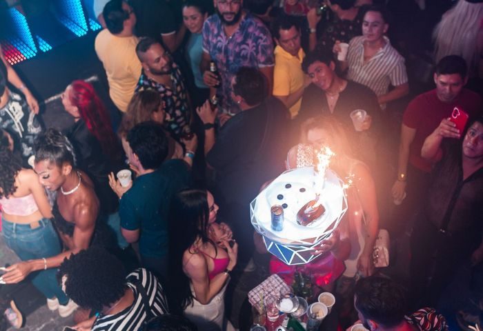 Crowded dance floor at The Back Door gay bar in Cancun. Waitress carries a tray with a flaming dessert. Gay nightlife travel.